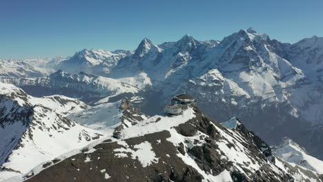 Volando-Sobre-El-Edificio-Del-Remonte-Con-Una-Concurrida-Terraza-En-La-Cima-De-Una-Montaña-Cubierta-De-Nieve