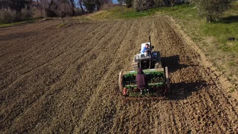 Gente-En-Tractor-Y-Sembradora-Trabajando-La-Tierra-Al-Atardecer,-Toma-Aérea