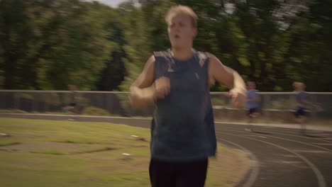 Runners-sprint-past-coach-on-school-track-during-practice-on-a-late-summer-afternoon