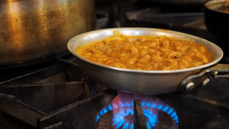 Indian-curry-bubbles-away-over-blue-flame,-simmering-sauce-over-heat,-slider----4K