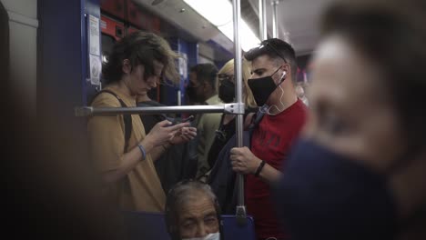 Un-Metro-En-La-Gran-Ciudad-De-Atenas,-Muchas-Personas-Con-Máscaras-Sentadas-Y-Paradas-En-El-Tren,-Un-Tipo-Está-Jugando-Con-Su-Teléfono-Móvil