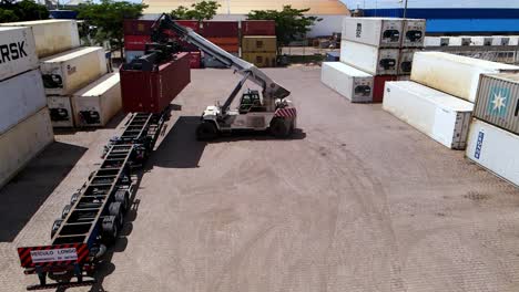 Red-shipping-container-placed-on-transport-truck-by-heavy-crane,-aerial-dolly