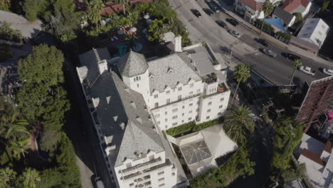 Aerial-pullback-on-the-Chateau-Marmont-in-Los-Angeles-with-the-swimming-pool,-Sunset-Boulevard-and-The-Hollywood-Hills-in-the-background