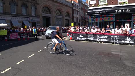 Grupo-De-Ciclistas-Cruzando-Una-Carretera-Bloqueada-Durante-El-Espectáculo-Al-Aire-Libre-De-Gumball-3000-Con-Autos-Deportivos-Modernos-De-Lujo