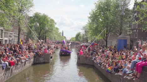 Menschenmenge-Versammelte-Sich-Um-Den-Amsterdamer-Kanal,-Um-Den-LGBTQ-Stolz-Zu-Unterstützen-Und-Zu-Feiern,-Während-Ein-Dekoriertes-Boot-Mit-Aktivisten-Vorbeifährt