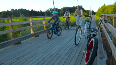 Zwei-Fahrräder-Auf-Einer-Hölzernen-Ländlichen-Brücke-Während-Des-Sonnenuntergangs-Und-Am-Abend,-Während-Einige-Leute-Mit-Ihren-Fahrrädern-Vorbeifahren