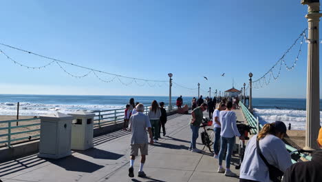 People-walking-along-Manhattan-Beach-Pier-on-a-sunny-day-with-the-ocean-in-the-background