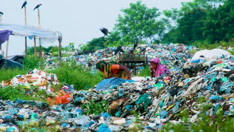 Frauen-Arbeiten-Unermüdlich-Auf-Einer-Großen-Verschmutzten-Mülldeponie-In-Bangladesch,-über-Ihnen-Fliegen-Schwarze-Krähen