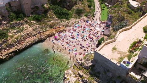 Gente-Disfrutando-En-La-Playa-De-Lama-Monachile-En-Polignano-A-Mare,-Mar-Adriático,-Apulia,-Italia---Disparo-De-Drone