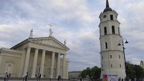 Vilnius-Cathedral-in-Lithuania-with-fluffy-white-clouds-in-sky-as-tourists-drive-past-along-road