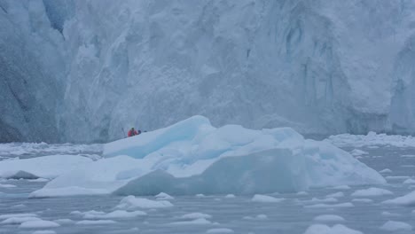 People-on-Polar-Expedition-Sailing-in-Boat-Under-Glacier-by-Pieces-of-Ice-on-Cold-Snowy-Day