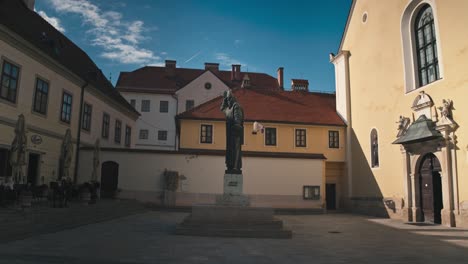 statue-of-Gregory-of-Nin-stands-in-a-charming-courtyard-in-Varaždin,-Croatia,-surrounded-by-historic-buildings-and-a-church-under-a-bright-blue-sky