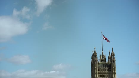 Slow-motion-footage-showcases-the-top-of-Victoria-Tower-in-Westminster,-with-a-flag-waving-against-a-clear-blue-sky