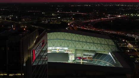 AERIAL:-in-front-of-the-Marriott-Marquis-with-Minute-maid-park-background,-night-in-Houston