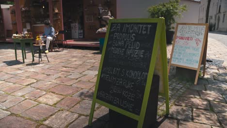 Chalkboard-signs-displaying-traditional-craft-products-and-prices-at-the-Market-of-Traditional-Crafts-in-Varazdin,-with-a-vendor-sitting-nearby