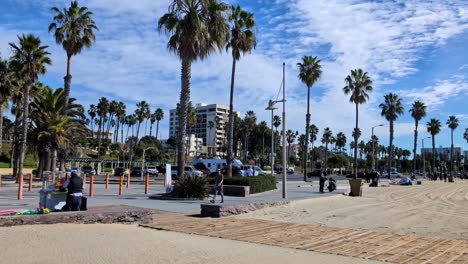 Beachfront-street-with-palm-trees,-static-shot-at-Venice-Beach,-People-walk-in-Californian-daylight