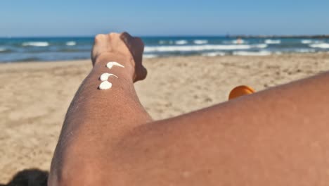 Close-up-of-a-person-applying-sunscreen-on-his-arm-at-the-beach