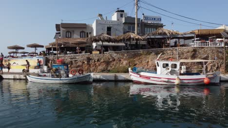 Drone-flying-near-the-water-surface-in-the-harbor-of-the-town-of-Sissi-in-Crete,-Greece---Fishing-boats-are-in-the-harbor-and-people-are-seen-jumping-into-the-water