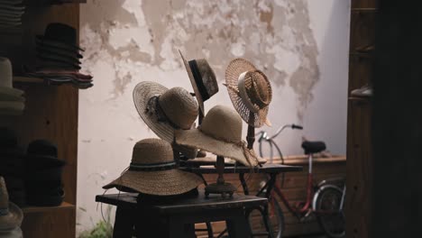 Straw-hats-on-display-at-Varaždin's-Market-of-Traditional-Crafts,-with-a-bicycle-and-rustic-wall-in-the-background