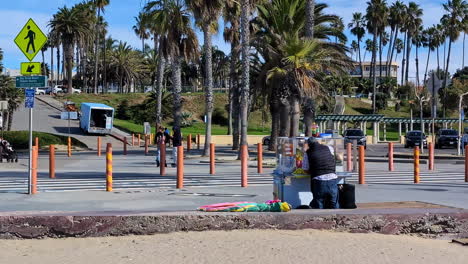 Vendor-setting-up-cart-near-crosswalk-and-palm-trees-on-a-sunny-day-at-Venice-Beach