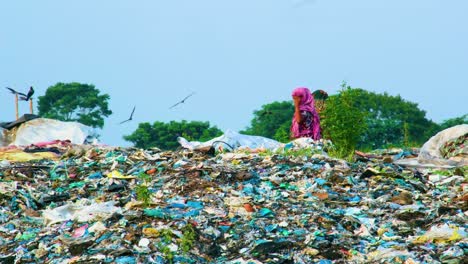 Frauen-Arbeiten-Auf-Einem-Berg-Verschmutzter-Mülldeponien-Mit-Endlosen-Mengen-An-Plastik-Und-Müll,-Während-Krähen-über-Ihnen-In-Bangladesch-Fliegen