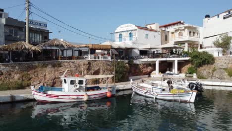 Drone-flying-near-the-water-surface-in-the-harbor-of-the-town-of-Sissi-in-Crete-Greece---Fishing-boats-are-in-the-harbor-and-beautiful-Greek-houses