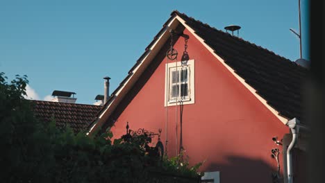 Charming-red-house-in-Varazdin-with-a-small-window-and-pulley-system,-surrounded-by-lush-greenery