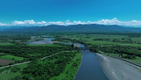 Vista-Aérea-De-Un-Río-Que-Fluye-A-Través-De-Un-Paisaje-Montañoso-Con-Valles-Verdes,-Capturando-La-Serena-Belleza-Natural