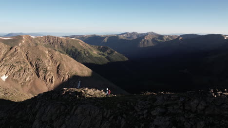 Aerial-View-of-Lonesome-Female-Hiker-Walking-Atop-of-Rocky-Hill-Above-Stunning-Mountain-Landscape