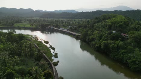 Idyllic-flyover-drone-shot-of-tropical-jungle-river-surrounded-by-lush-greenery-and-quaint-villages-in-Catanduanes,-Philippines