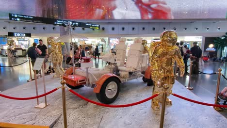 Space-moon-buggy-and-astronaut-display-with-people-walking-in-Hamad-International-Airport-in-Doha,-Qatar