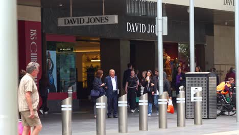 People-shopping-at-the-David-Jones-flagship-store-in-bustling-downtown-Melbourne-city-with-pedestrians-strolling-on-Bourke-Street-Mall,-slow-motion-static-shot