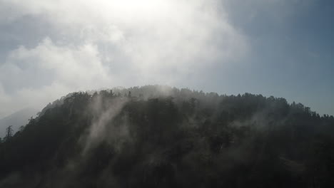 Slow-moving-drone-shot-of-fog-rolling-over-a-mountain-top