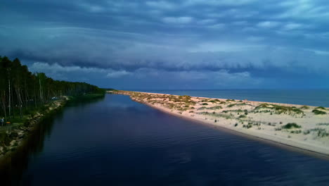 Pool-of-calm-water-reflects-tall-trees-on-edge-of-beach-with-sandy-dunes-and-shallow-grass,-aerial-ascend