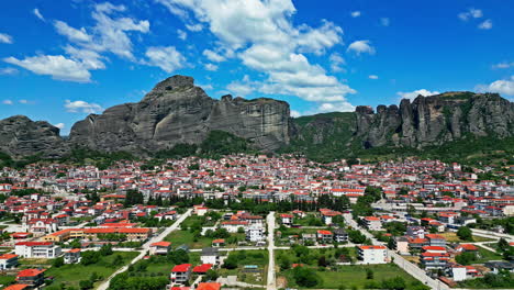 Aerial-drone-flight-over-a-city,-buildings-with-red-roofs-and-mountains-in-the-background-on-a-sunny-day,-copy-space-and-slowmotion