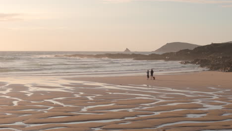 People-enjoy-Treyarnon-beach-sunset-view-over-ocean-at-low-tide,-aerial-tracking