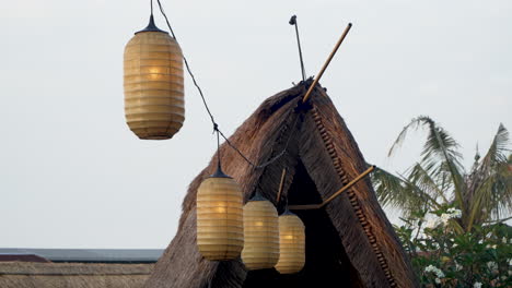 Esoteric-Lamps-Swinging-Hang-Between-Thatched-Rural-Hut-Roofs,-Bali-Traditional-Decor-and-Architecture,-Indonesia