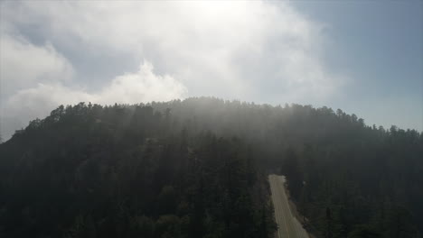 Slow-tilting-up-drone-shot-of-fog-rolling-over-a-mountain-top-and-an-empty-road