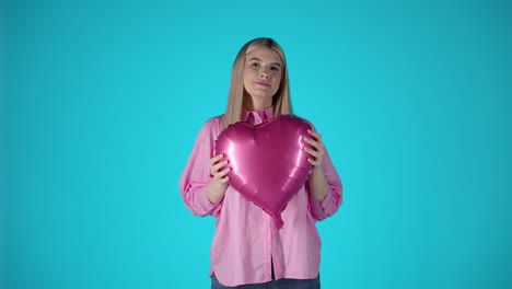 Mujer-Rubia-Sosteniendo-Un-Globo-Morado-En-Forma-De-Corazón,-Humor-De-San-Valentín-Con-Fondo-De-Color-Azul,-Foto-De-Estudio