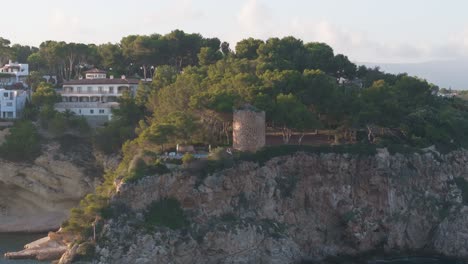 Aerial-view-of-coastal-city-and-historic-tower-on-cliff-edge,-Mallorca