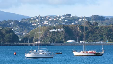 Harbour-view-of-yachts-and-iconic-windy-Wellington-sign-landmark-in-the-hills-in-capital-city-of-Wellington,-New-Zealand-Aotearoa