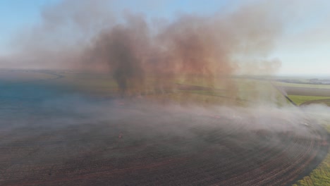 Aerial-pan-of-a-controlled-fire-releasing-a-lot-of-smoke-in-the-air,-strategically-used-to-manage-sugarcane-farmlands