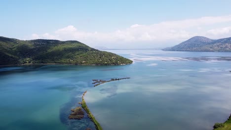 Stunning-aerial-view-of-Butrint-National-Park,-featuring-lush-green-hills-and-crystal-clear-blue-waters-in-Albania