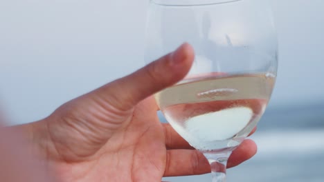 Glass-of-white-wine-is-poured-with-blue-ocean-backdrop,-detailed-closeup