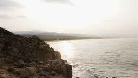 Drone-soars-along-edge-of-eroded-cliffs-with-ocean-spray-erupting-at-sunset-in-Puerto-Escondido-Oaxaca-Mexico