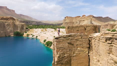 Band-E-Amir-Lake-With-Man-On-Top-Of-A-Cliff-In-Bamyan-Province,-Afghanistan---Drone-Shot