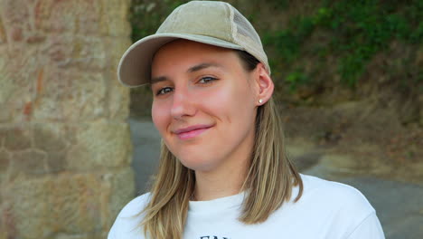 Portrait-of-a-pretty-young-blonde-woman-with-cap-smiling-shyly-at-camera