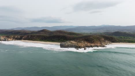 Drone-approaches-sandy-bay-as-waves-crash-on-shores-of-Puerto-Escondido-Oaxaca-Mexico