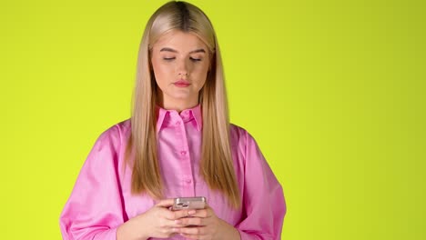 Blonde-Frau-Hält-Ein-Smartphone,-Scrollt-Auf-Dem-Touchscreen-Und-Lächelt,-Farbenfrohe-Studioaufnahme