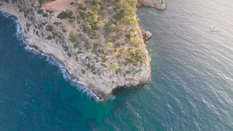 Aerial-ascend-over-limestone-cliff-near-tropic-turquoise-water,-Mallorca